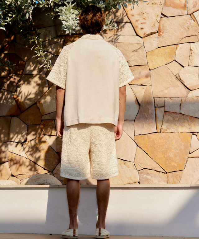 beige button-up shirt with lace details and matching lace shorts, set against a stone backdrop.