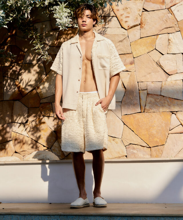 beige button-up shirt with lace details and matching lace shorts, set against a stone backdrop.