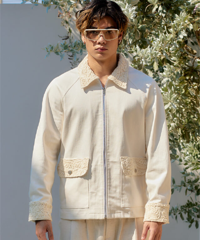 Close-up of a model wearing a beige zip-up jacket with intricate lace accents on the collar and pockets, set by a poolside
